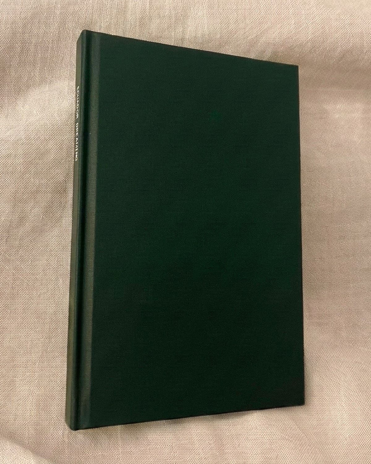 A forest green linen wrap photo book standing on cream linen, its title foil stamped along the spine