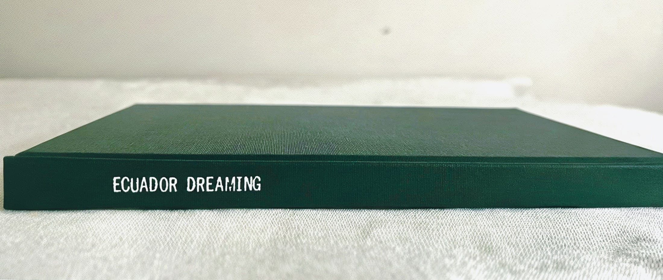 A forest green linen wrap photo book with its title foil stamped along the spine