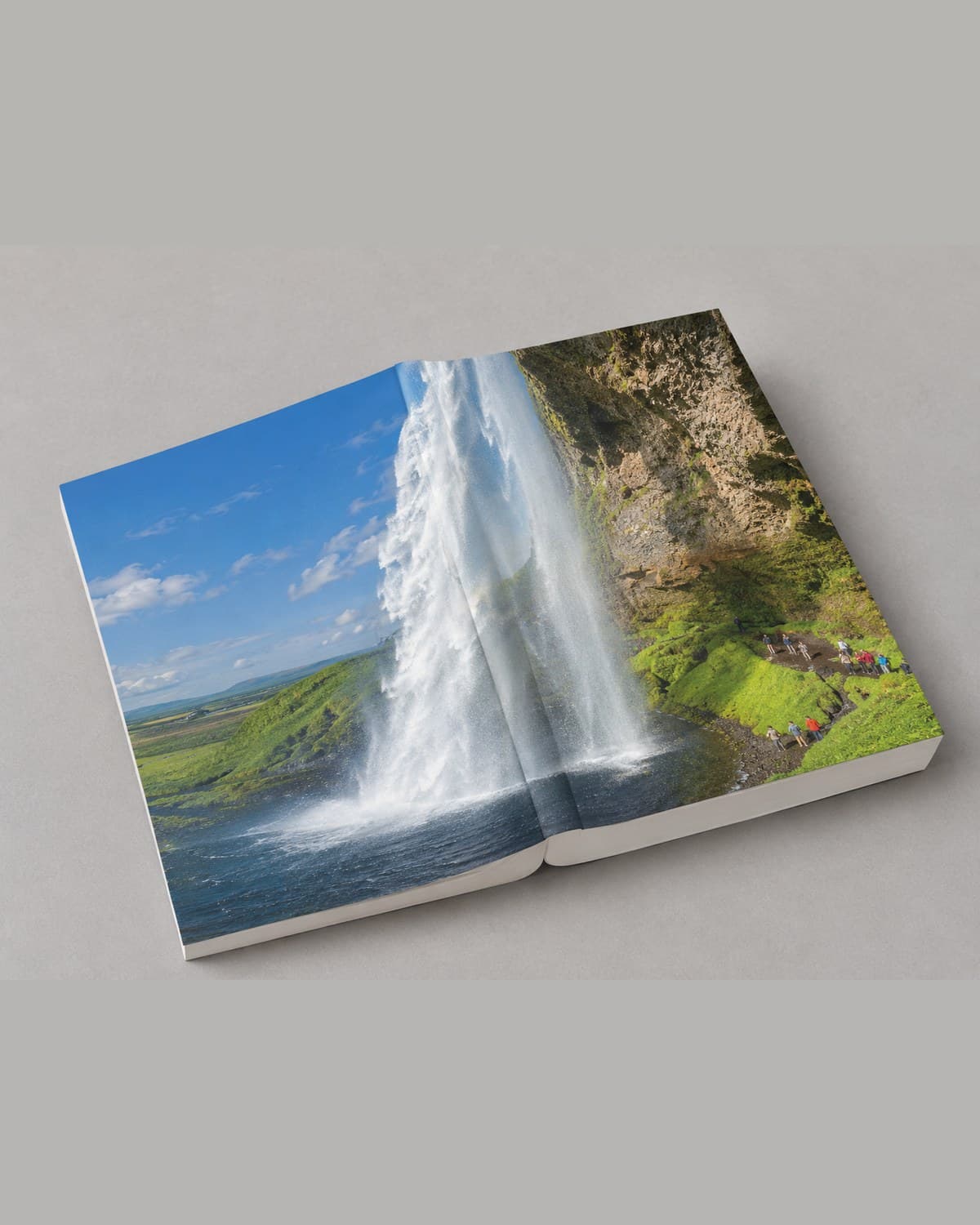 An AI-generated mockup of a softcover photo book lying open, showing a waterfall photograph across both pages